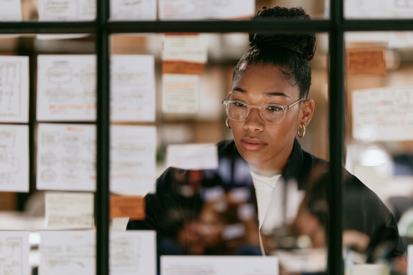 A leader working behind a glass wall covered in notes and diagrams.